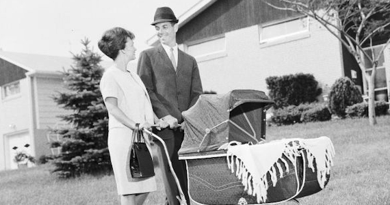 a man and woman pushing a crib in a suburban neighborhood